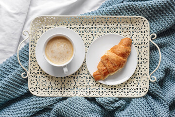 Tray with cup of coffee and croissant on knitted plaid