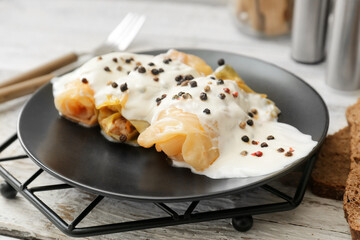 Plate with tasty stuffed cabbage rolls and sauce on light wooden background