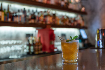 Beautiful yellow citrus cocktail on the bar counter with ice and decoration with an orange piece and mint leaves