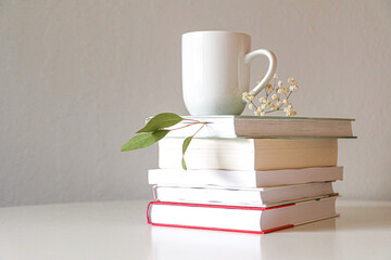 a white ceramic cup with tea stands on a stack of books on a light background 