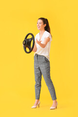 Young woman with steering wheel on yellow background