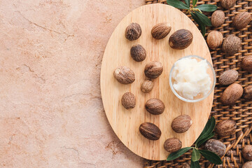 Wooden board with shea butter and nuts on color background, closeup