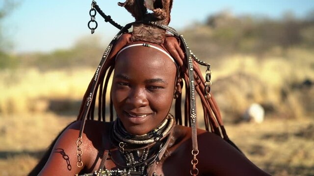 Beautiful Himba woman smiling, wearing traditional jewellery and headdress in her village near Kamanjab in northern Namibia, Africa, slow motion shot.