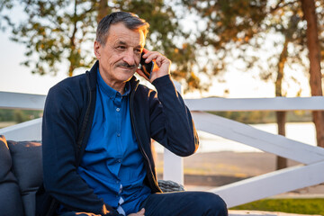 Senior caucasian man with mustaches using mobile phone while sitting outdoor at cafe or restaurant in autumn evening copy space real people