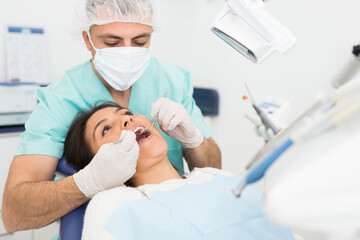 Dentist man examining a latin female patient teeth with dental tools - mirror and probe