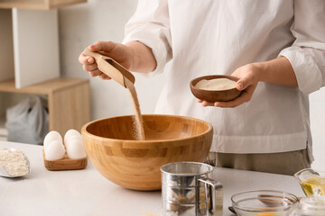 Female chef adding dry yeast in bowl on kitchen table, closeup