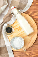 Glass cup of tasty Charcoal Latte and bottle with milk on wooden background
