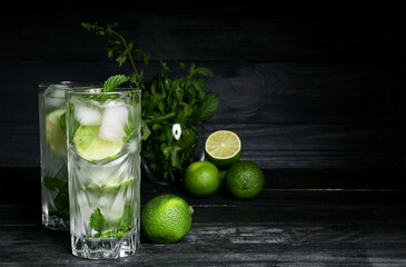 Glasses of fresh mojito, limes and mint on dark wooden background
