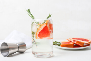 Glass of cold gin tonic and grapefruit slices on light background