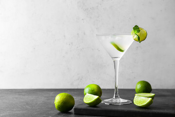 Glass of tasty margarita cocktail and limes on light background