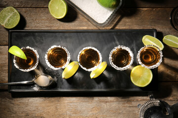 Shots of tasty tequila with lime on wooden background