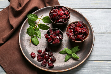 Bowls with tasty dried cranberries on color wooden background, closeup