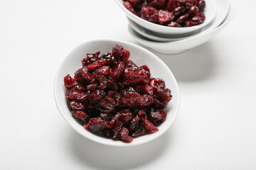 Bowl with tasty dried cranberries on light wooden background, closeup