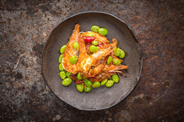 Pad Ped Sator Goong, Thai food, Prawns and Stink Beans Fried with Red Curry Paste in wabi sabi style plate on rusty texture background, top view, bitter bean, twisted cluster bean, stink bean