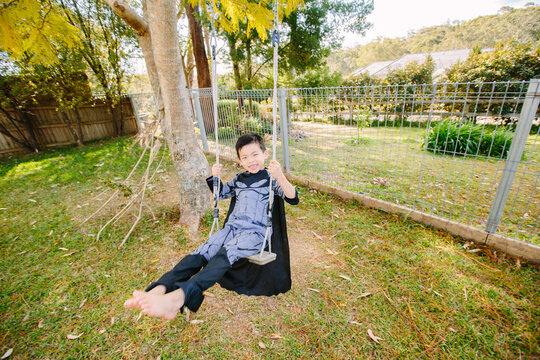 Little boy dressed as batman playing in the garden on a swing on a sunny day