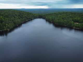 Over Buckskin Lake on an overcast, summer afternoon with rain falling in the distance. Aerial above expansive wilderness of crown land located in the Tory Hill area of Highlands East, Ontario, Canada.