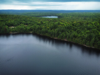 Fototapeta premium Over Buckskin Lake on an overcast, late summer afternoon with Monrock Lake in the distance. Aerial above crown land wilderness in the Tory Hill area of Highlands East, Ontario, Canada.