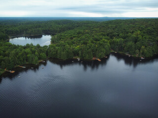 Fototapeta na wymiar Over Buckskin Lake and Lower Buckskin Lake on a cloudy summer afternoon. Aerial above cottages in the wilderness of crown land located in the Tory Hill, Highlands East, southern Ontario, Canada.