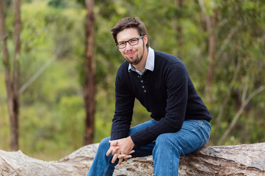 Happy young man in his twenties sitting on a log outside