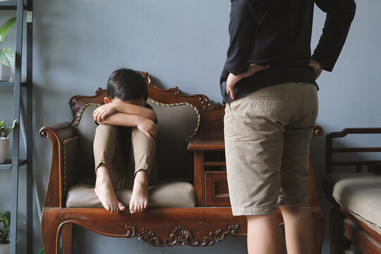 A Little Asian boy crying on the sofa while being scolded by someone stands in front of him. Bullying, discrimination, and racism concept