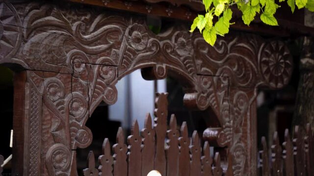 Brown-colored wooden gate with Hungarian patterns, half-covered with foliage.