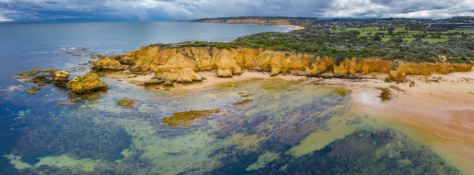 Aerial view of sea cliff jutting out into a calm bay under dark skies