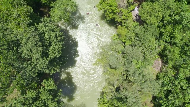 Drone aerial footage of flowing rainforest river lined with lush green trees and foliage with people riding down stream in floating donuts. Rio Cahabon, Guatemala near Semuc Champey National Park.