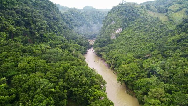 Drone aerial panorama of flowing rainforest river valley lined with lush green trees surrounded by dense jungle hillsides and mountains. Rio Cahabon near Semuc Champey, Guatemala.