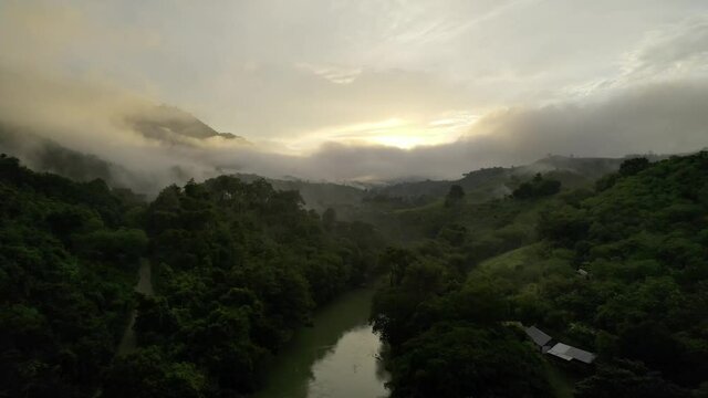 Drone aerial footage of dusk sunset over misty and cloudy rainforest valley and river lined with lush dark green trees near Semuc Champey National Park, Guatemala.