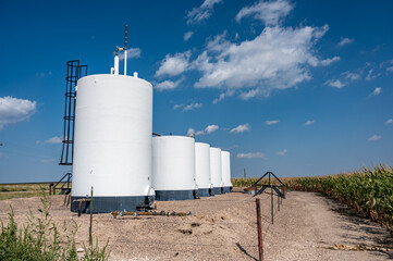crude oil storage tanks with secondary containment and fencing in a rural corn field