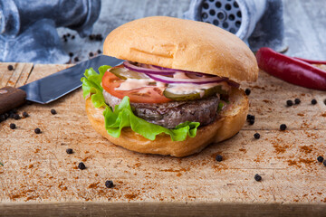 burger on wooden board with knife and grinder with pepper