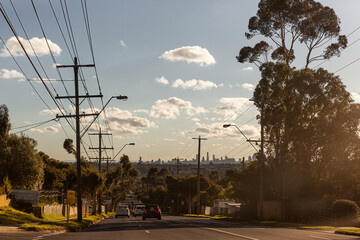 Cars driving along suburban street with Melbourne city skyline in background.
