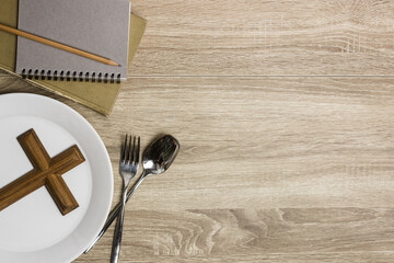 cross on a white plate with bible and notebook on a wooden table