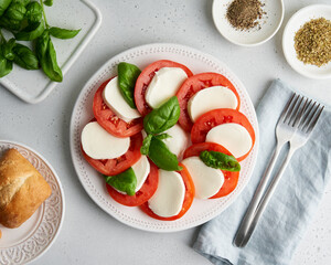 Traditional recipe of italian caprese salad with sliced tomatoes, mozzarella, basil, oregano, pepper, ciabatta. Horizontal flat lay of delicious mediterranean appetizer. Fresh vegetarian meal