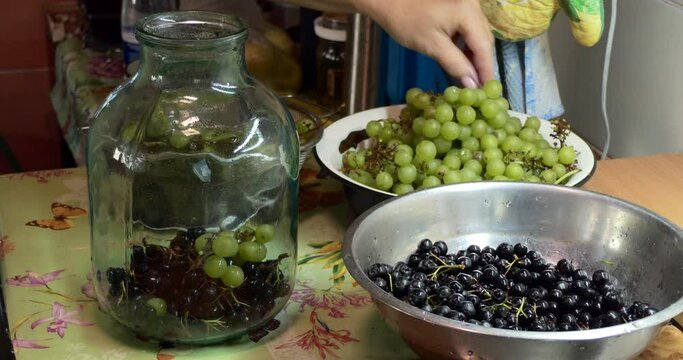 Home canning. A woman puts a rowan chokeberry and grapes in a glass jar for making canned compote.  Close-up. Siberia.
