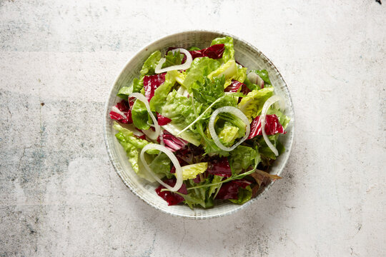 close up shot of a green salad in a bowl on top of a rustic grey tabletop
