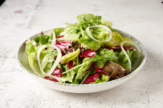 green salad in a bowl on top of a rustic grey tabletop with onion rings