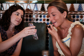 Two friends helping to put on makeup in a hotel cafeteria