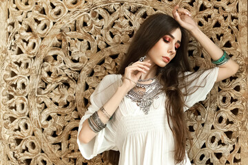 Beautiful girl in white dress and stylish jewelry inside room middle eastern interior
