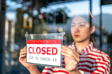 An upset Local small business owner woman or waitress is putting the sign for "sorry we closed" in front of the cafe, coffee shop, or retail store glass door cause lockdown quarantine due to covid-19