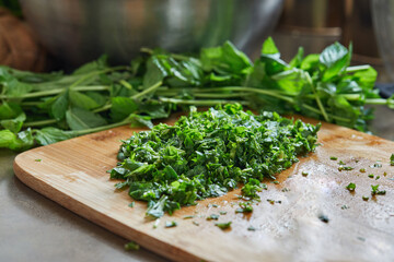 Chef cuts basil according to the recipe for cooking on wooden board in the kitchen