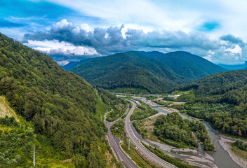 aerial panorama of the gorge in the valley of the mountain river Mzymta between the forested green mountains of the Caucasus. Highway and railway in the distance