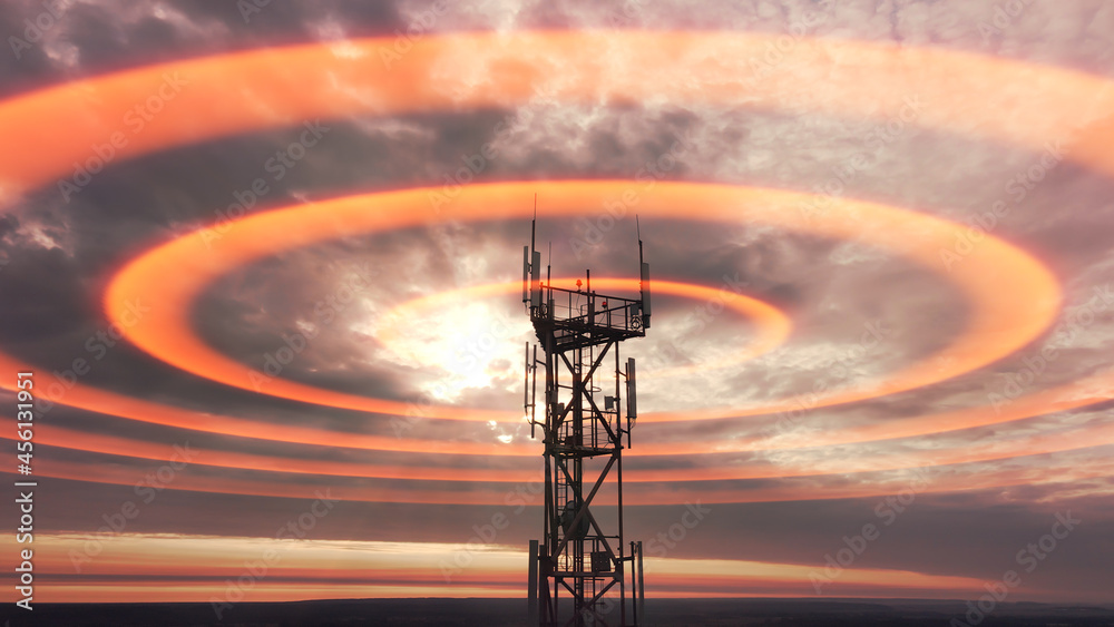 Wall mural Wireless telecom radiation with aerial footage. Silhouette of telecommunication tower construction with antenna dishes on red sunset. Mobile digital radio waves animation from the high cellular mast.