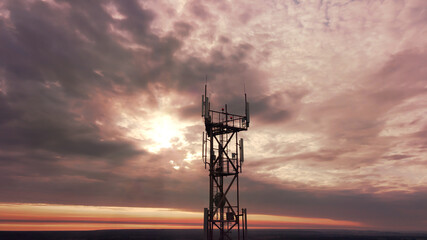 Telecommunication tower construction with cellular satellite antennae dishes on the epic red sunset sky on background. Innovation wireless broadcast network technology transmit signal by radio wave.