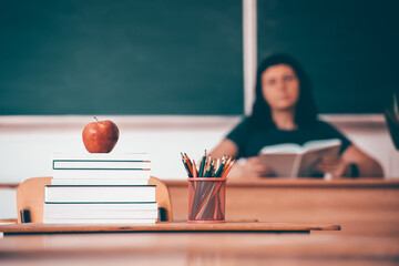 Pencils, apple and books, teacher and blackboard in the background. Education concept.