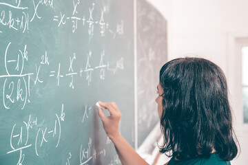 Female student or teacher in the classroom writing on chalkboard mathematical equations