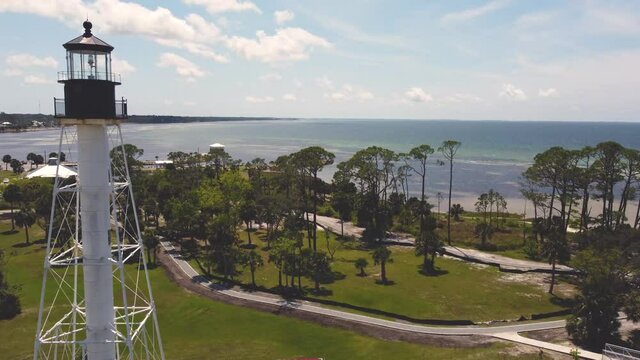 Lighthouse along the sunny Florida coastline with views of the ocean, sandy beaches, and green palm trees.  Warm inviting adventurous 4k aerial footage of  shoreline.