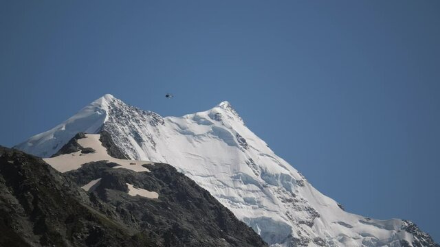 From the ground static shot of a helicopter flying over snovy mountains on a clear sunny day in 4K, beautiful scenery in New Zealand.