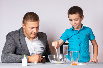 Chemistry education and training concept. Close-up of a boy and his dad doing a home chemical experiment, making slime from glue, sodium tetraborate and dyes