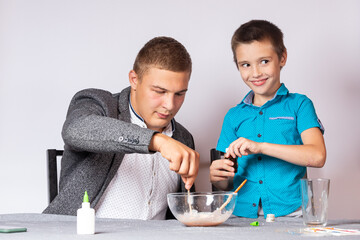 Chemistry education and training concept. Close-up of a boy and his dad doing a home chemical experiment, making slime from glue, sodium tetraborate and dyes